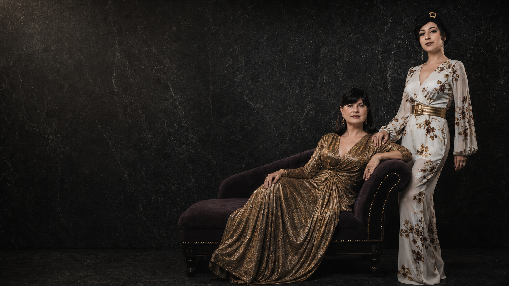 Two women in elegant dresses sitting on a dark background