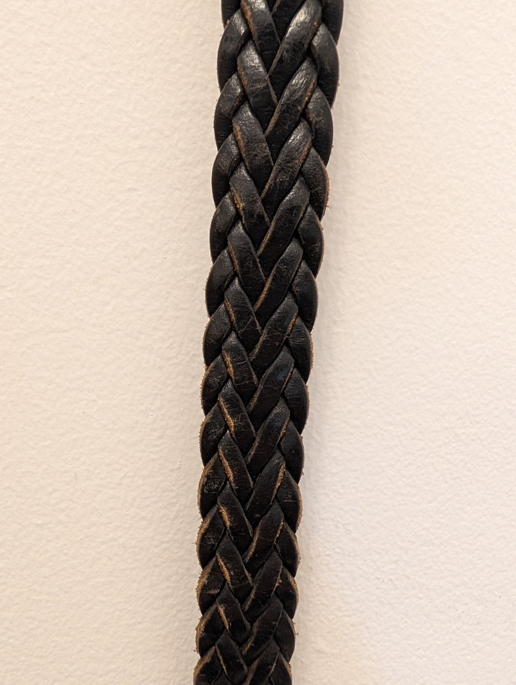 A close-up of a thick black braided leather strap or cord, vertically oriented against a plain off-white background.