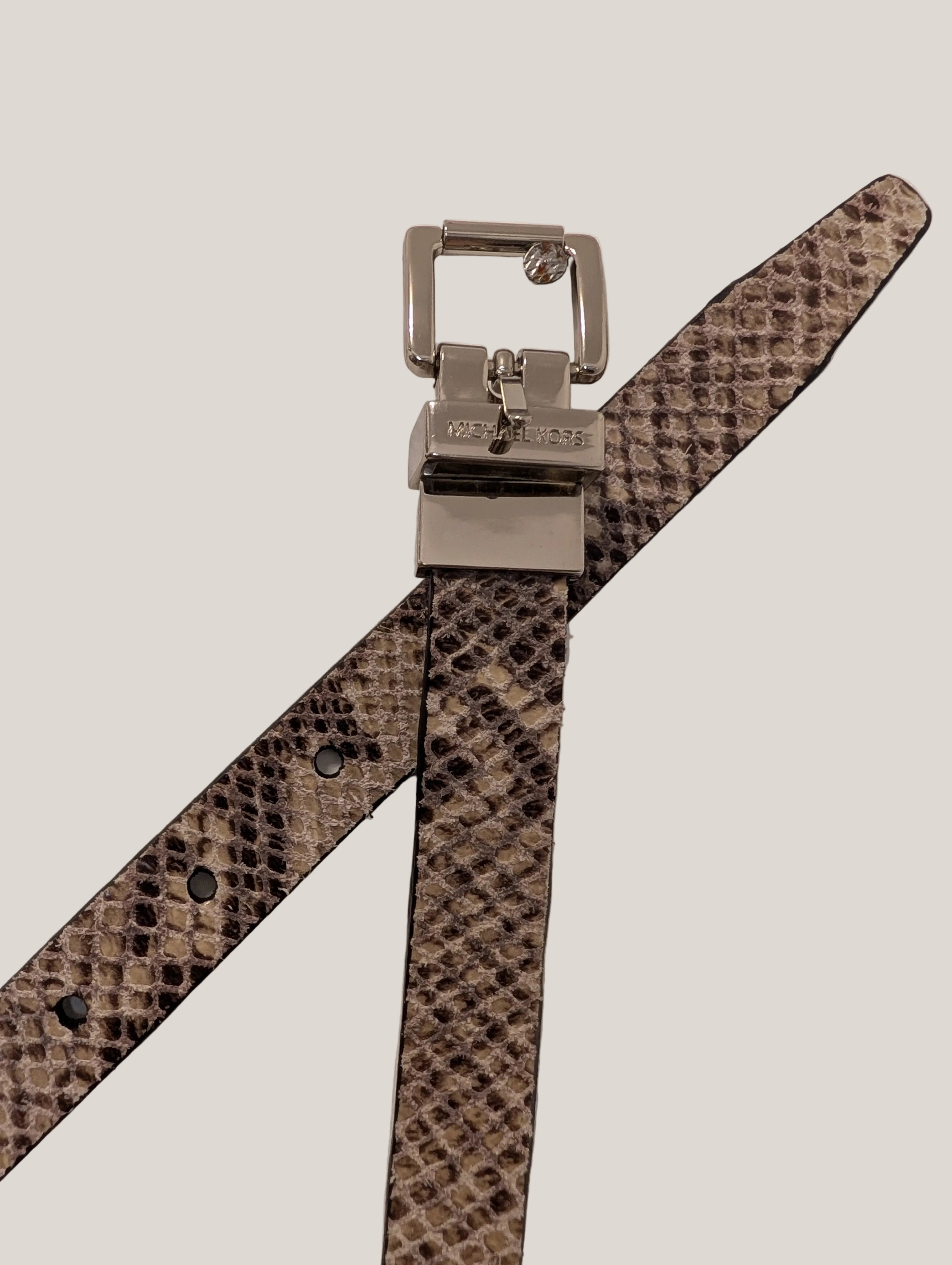 A snakeskin-patterned leather belt with a silver-tone metal buckle, laid flat on a textured off-white background.