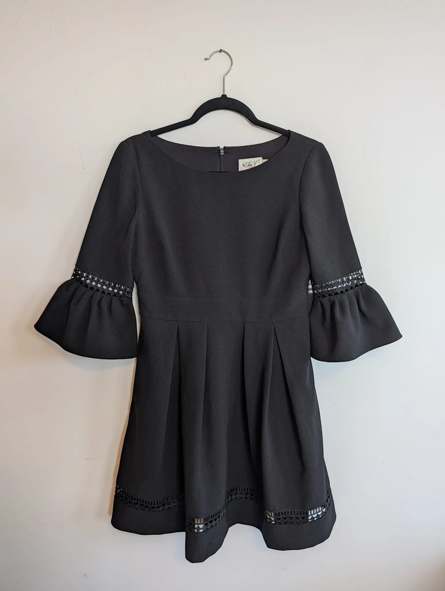 Nu-Nv Clothing black A-line mini dress with pleated skirt, bell sleeves, and intricate lace hem detailing.