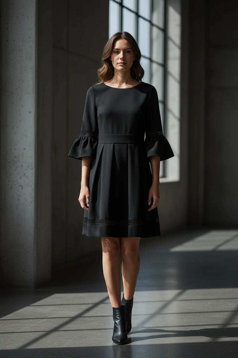Model wearing a Nu-Nv Clothing black A-line mini dress with pleated skirt, bell sleeves, and lace hem details.