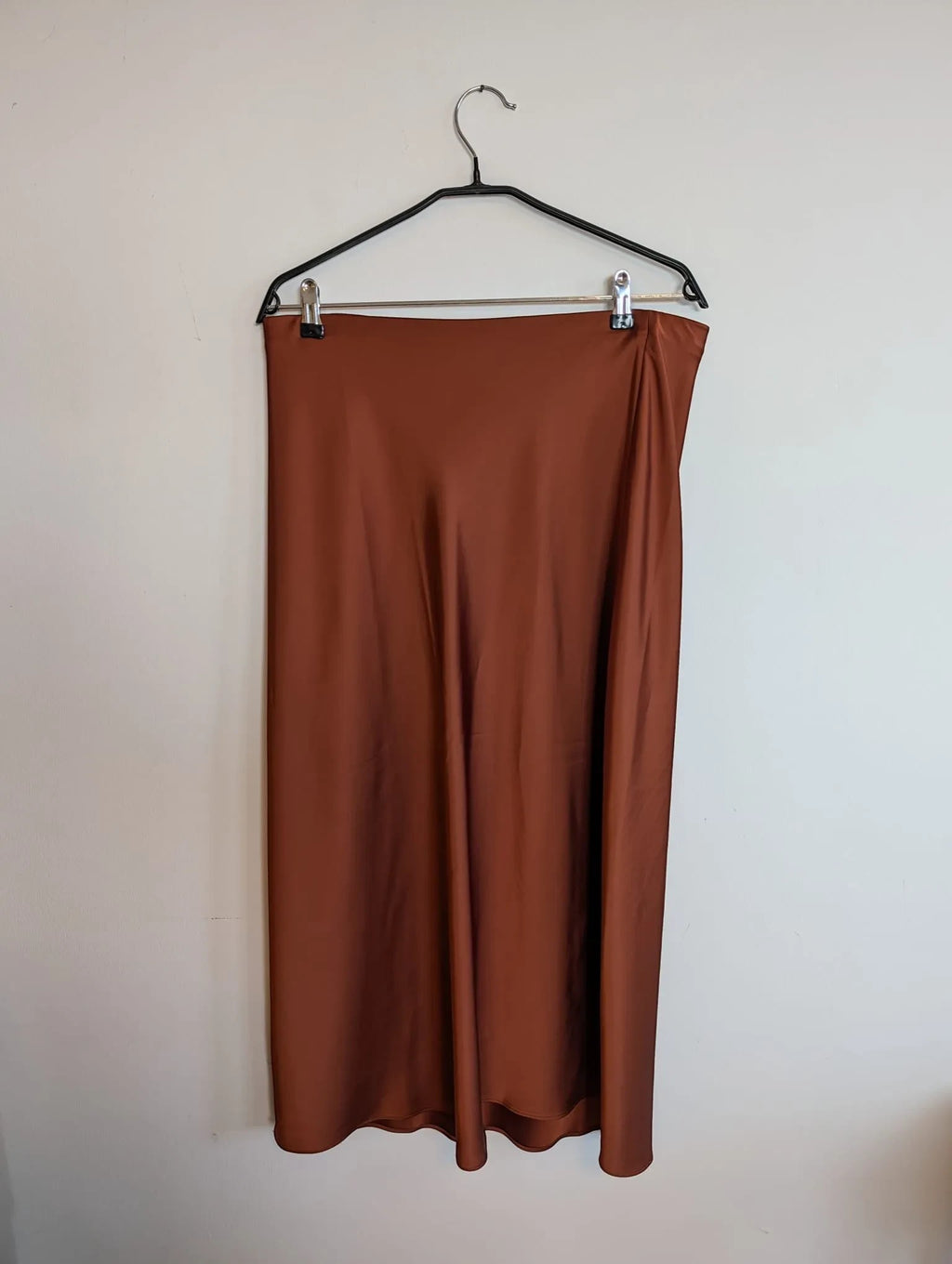 Nu-Nv Clothing brown satin midi skirt with a fluid bias-cut silhouette and lustrous finish hanging on a hanger.