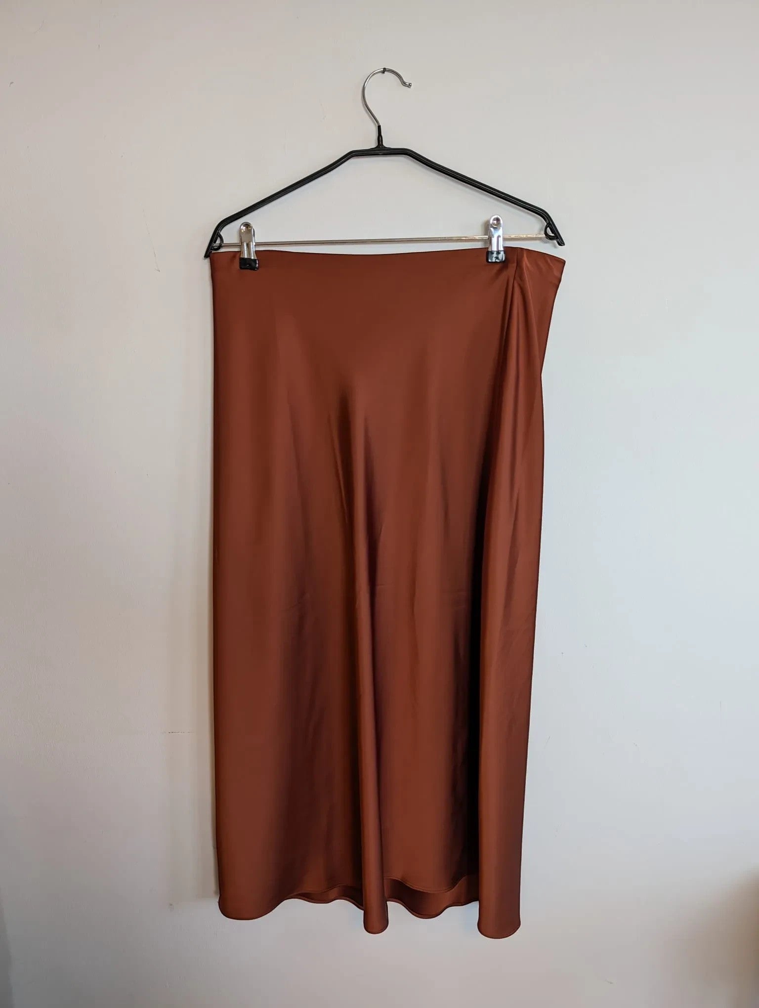 Nu-Nv Clothing brown satin midi skirt with a fluid bias-cut silhouette and lustrous finish hanging on a hanger.