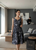Model wearing a Nu-Nv Clothing charcoal floral midi dress with a structured bodice and pleated skirt in a modern room.
